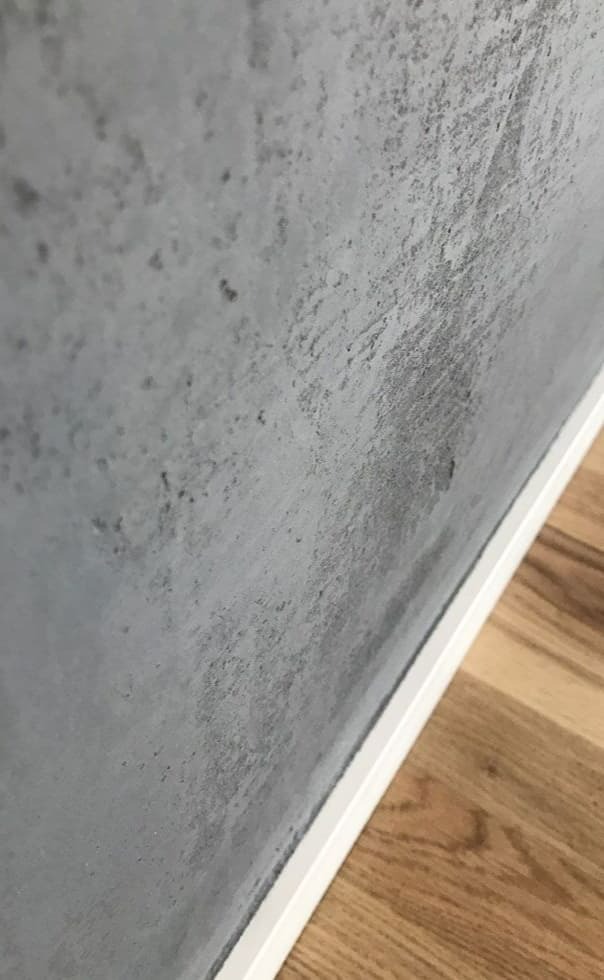 Szara ściana z efektem betonu architektonicznego, wykończona białą listwą przypodłogową i panele podłogowe w odcieniach brązu, ujęcie z bliska.