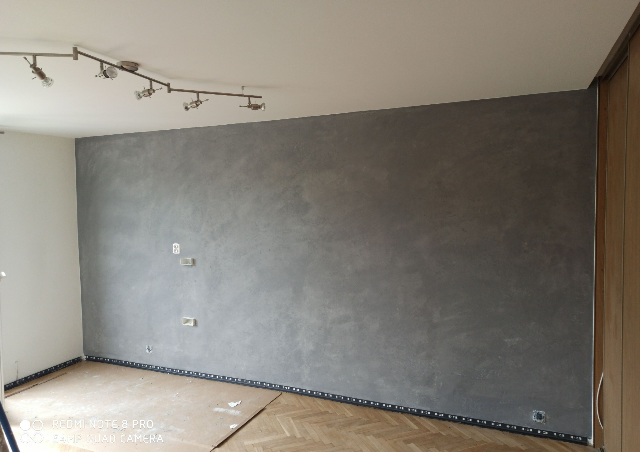 Pokój po wykonaniu gładzi w odcieniach szarości, zabezpieczony taśmą przy podłodze, widoczna instalacja elektryczna i parkiet w jodełkę.