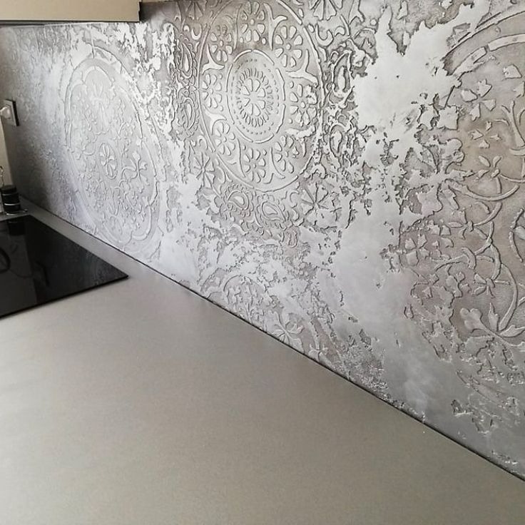Dekoracyjna ściana w kuchni z efektowną, srebrzystą fakturą i ornamentami kwiatowymi oraz motywami mandali, widoczna nad blatem kuchennym i płytą grzewczą.