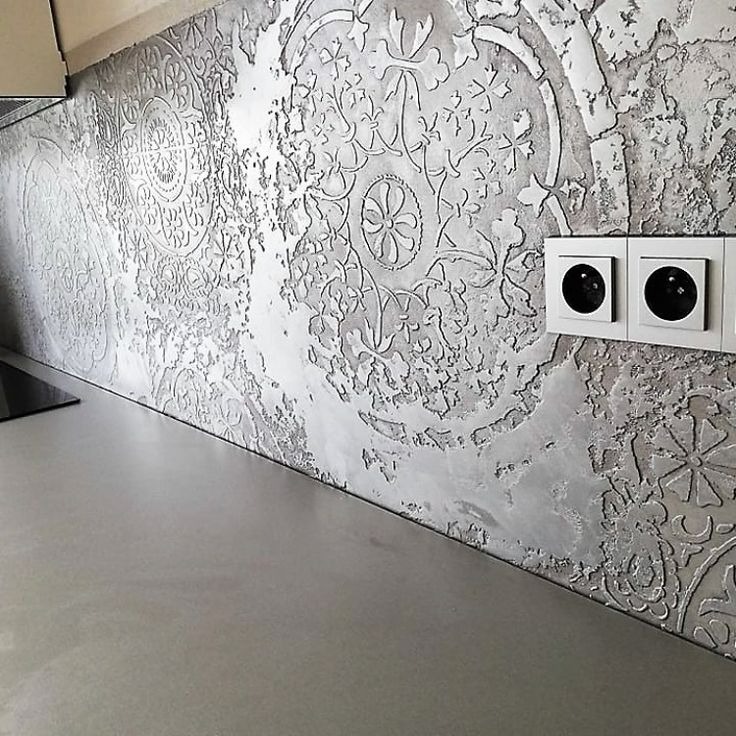 Dekoracyjna ściana w kuchni z fakturą i wzorem kwiatowym, gniazdka elektryczne na ścianie, szara powierzchnia blatu.