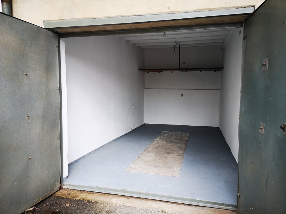 Wnętrze pustego, odświeżonego magazynu z szarą podłogą, białymi ścianami i otwartymi, stalowymi drzwiami na zewnątrz.