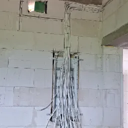 Rozdzielnica elektryczna w surowym stanie, z poprowadzonymi przewodami w ścianie z betonu komórkowego, widoczne drewniane elementy stropu.