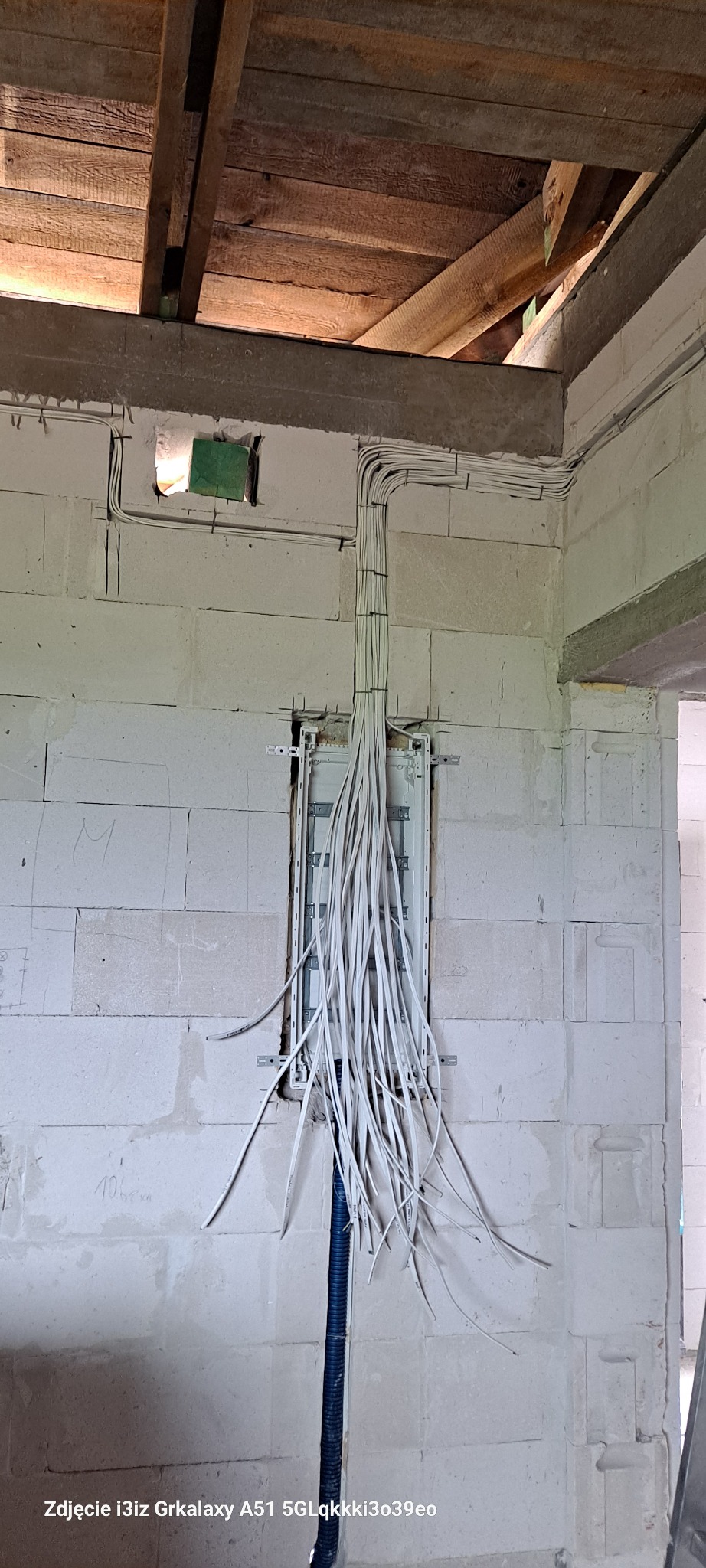 Rozdzielnica elektryczna w surowym stanie, z poprowadzonymi przewodami w ścianie z betonu komórkowego, widoczne drewniane elementy stropu.