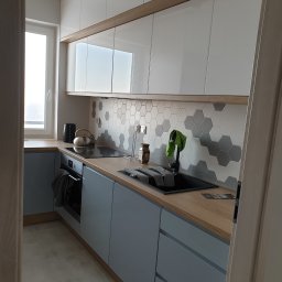 Illia Ivanov wykończenie wnętrz - Nowoczesna kuchnia z szarymi szafkami, drewnianym blatem i heksagonalnymi płytkami na ścianie, widok zza framugi drzwi.