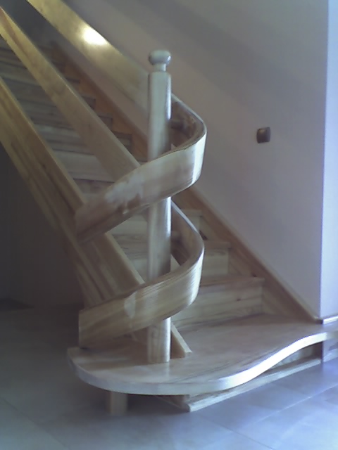 Drewniane schody z zakręconą balustradą, wykonane na zamówienie z jasnego drewna, widoczne z dołu.