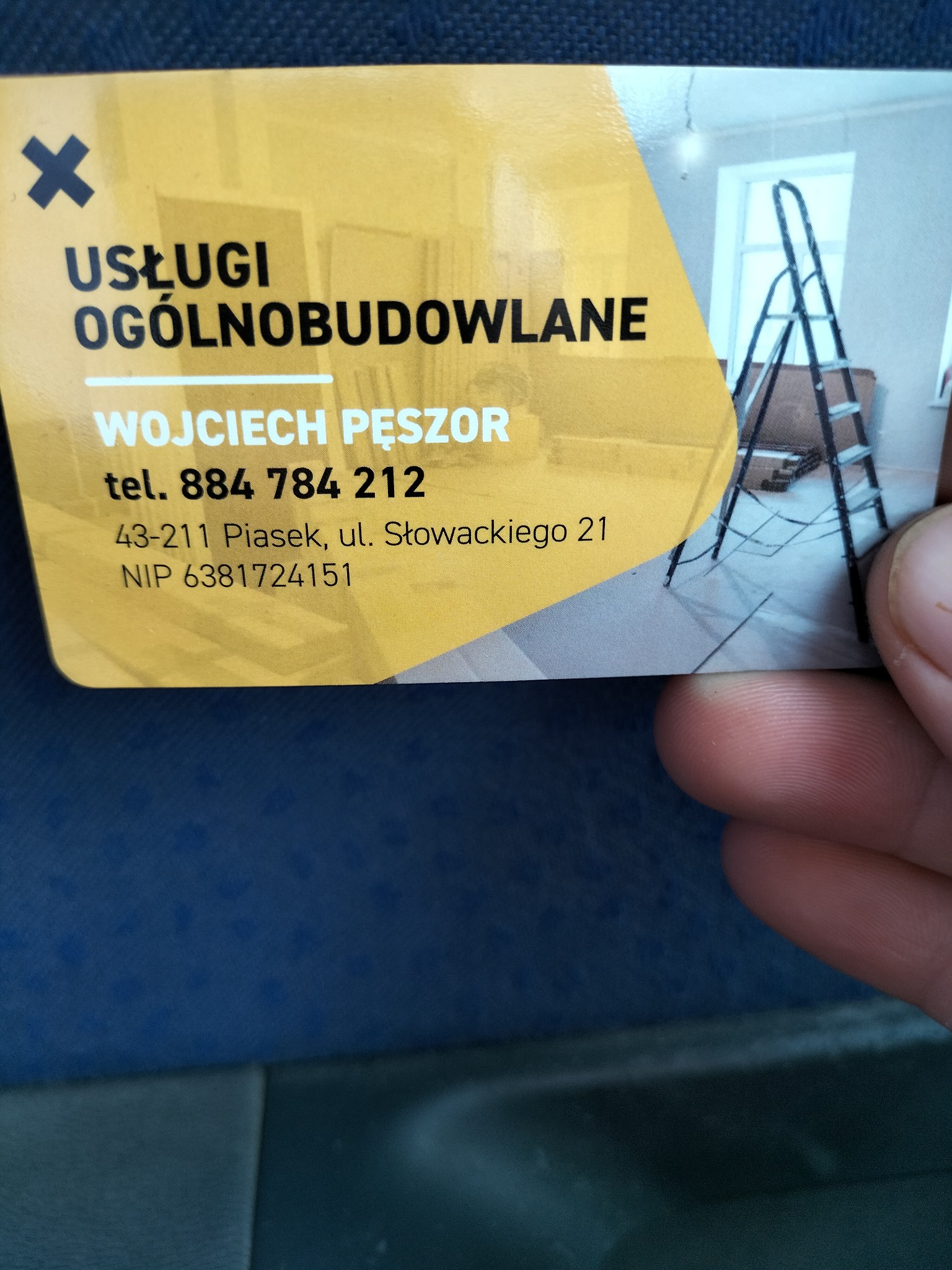 Wizytówka firmy Wojciech Pęszor Usługi Ogólnobudowlane z adresem i numerem telefonu, w tle fragment zdjęcia wnętrza z drabiną malarską.