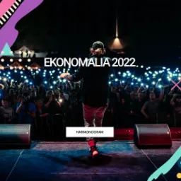 Scena podczas wydarzenia 'Ekonomia 2022', z tyłu tłum ludzi z podniesionymi telefonami, oświetlony reflektorami, na pierwszym planie głośniki i sylwetka osoby na scenie, całość wzbogacona...