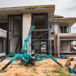 PM Technika Okienna - Montaż okien w surowym domu jednorodzinnym przy użyciu mini żurawia dekarskiego Matplast, widoczne przygotowane otwory okienne i rusztowania.