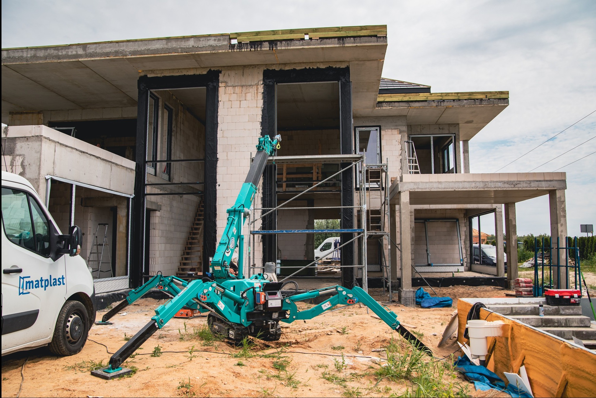 Montaż okien w surowym domu jednorodzinnym przy użyciu mini żurawia dekarskiego Matplast, widoczne przygotowane otwory okienne i rusztowania.