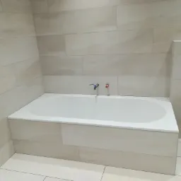 Wykończona łazienka z wanną obudowaną płytkami imitującymi kamień, bateria jeszcze nie podłączona, widoczne przyłącza wody.