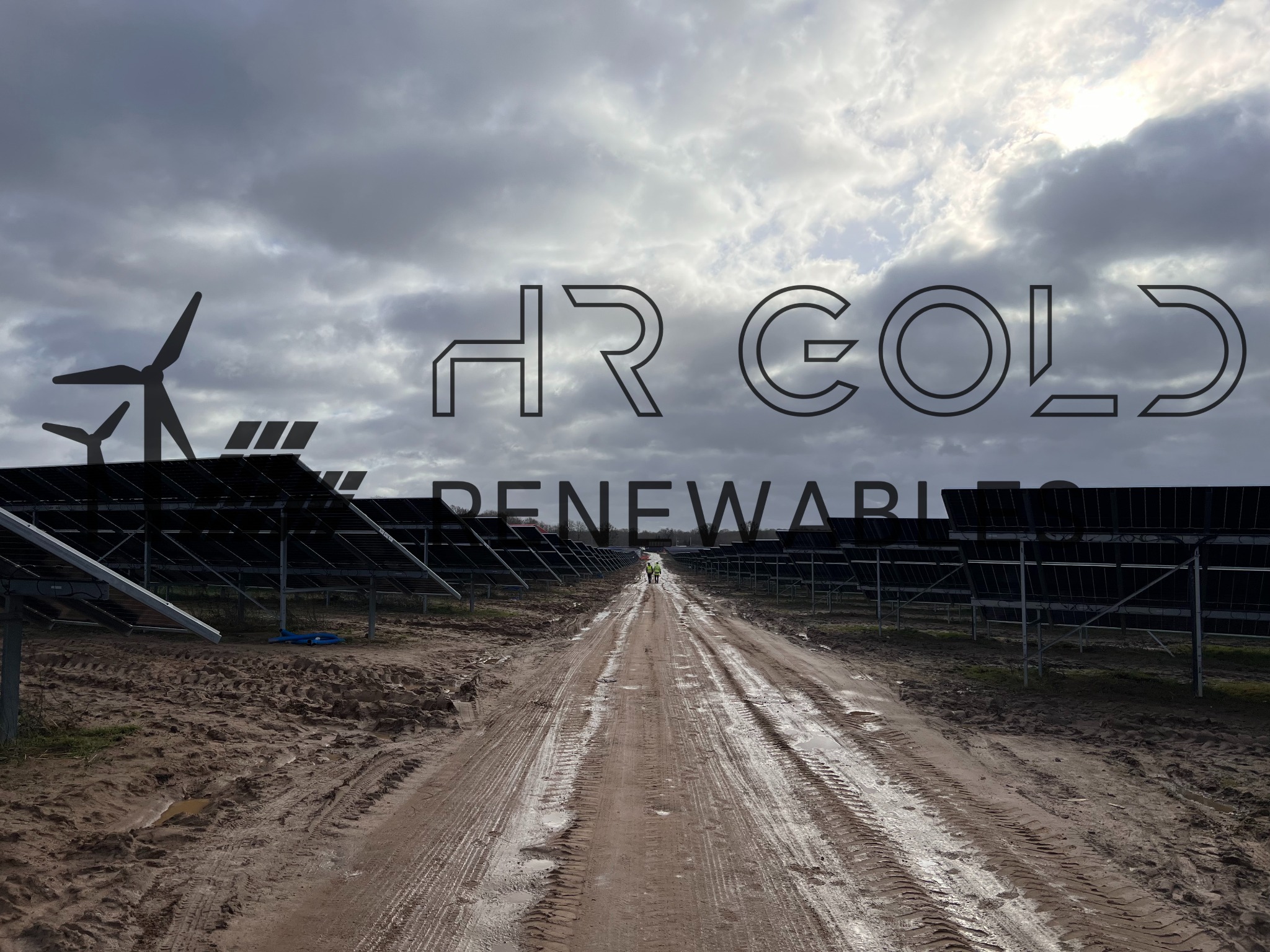 Instalacja farmy paneli słonecznych w pochmurny dzień, widoczna turbina wiatrowa w tle, błotnista droga dojazdowa z dwoma osobami w oddali, na zdjęciu widoczne logo firmy HR Gold Renewables.