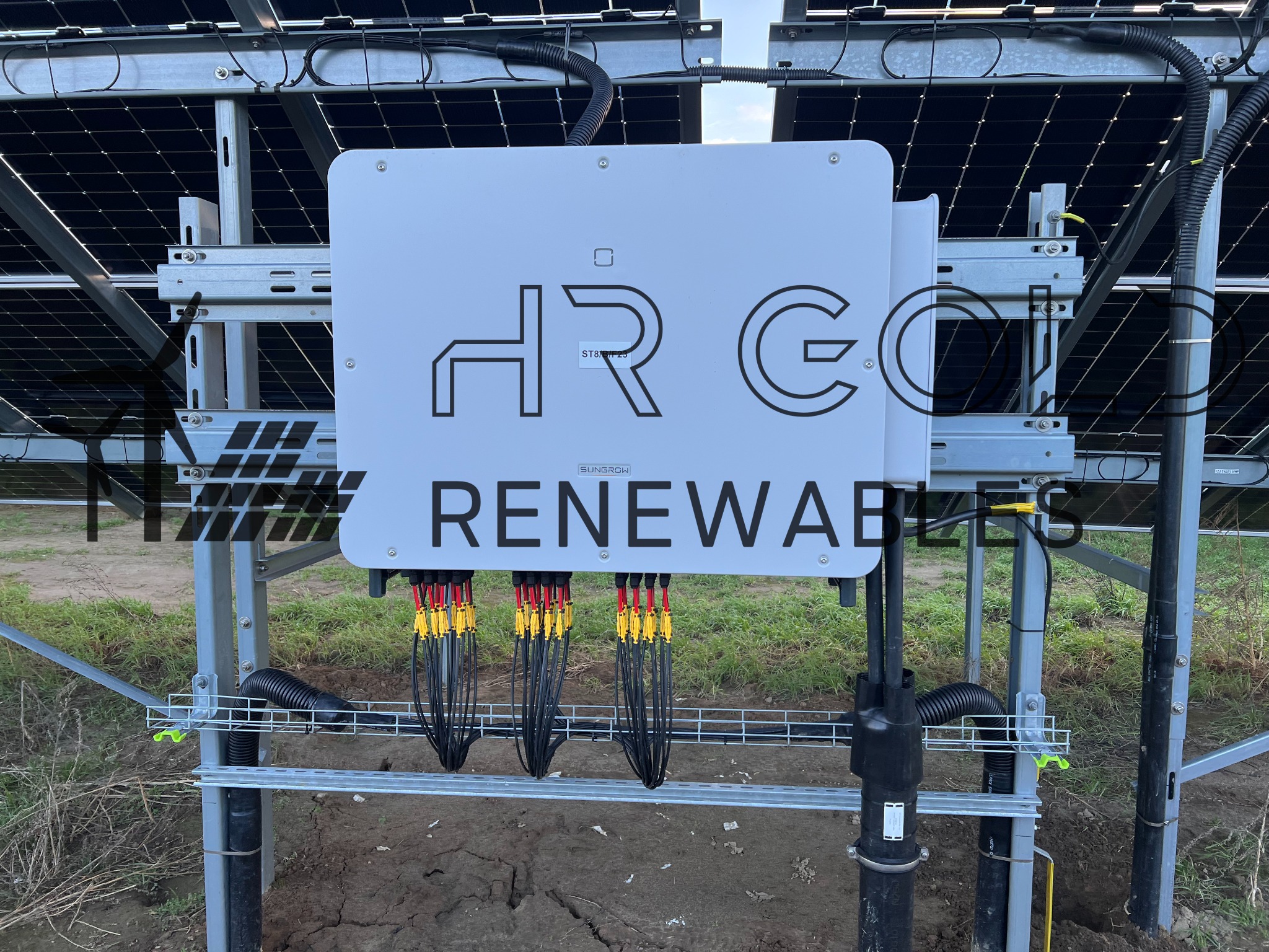Inwerter solarny Sungrow HRG Renewables zamontowany na metalowej konstrukcji, z widocznymi kablami i panelami słonecznymi w tle.