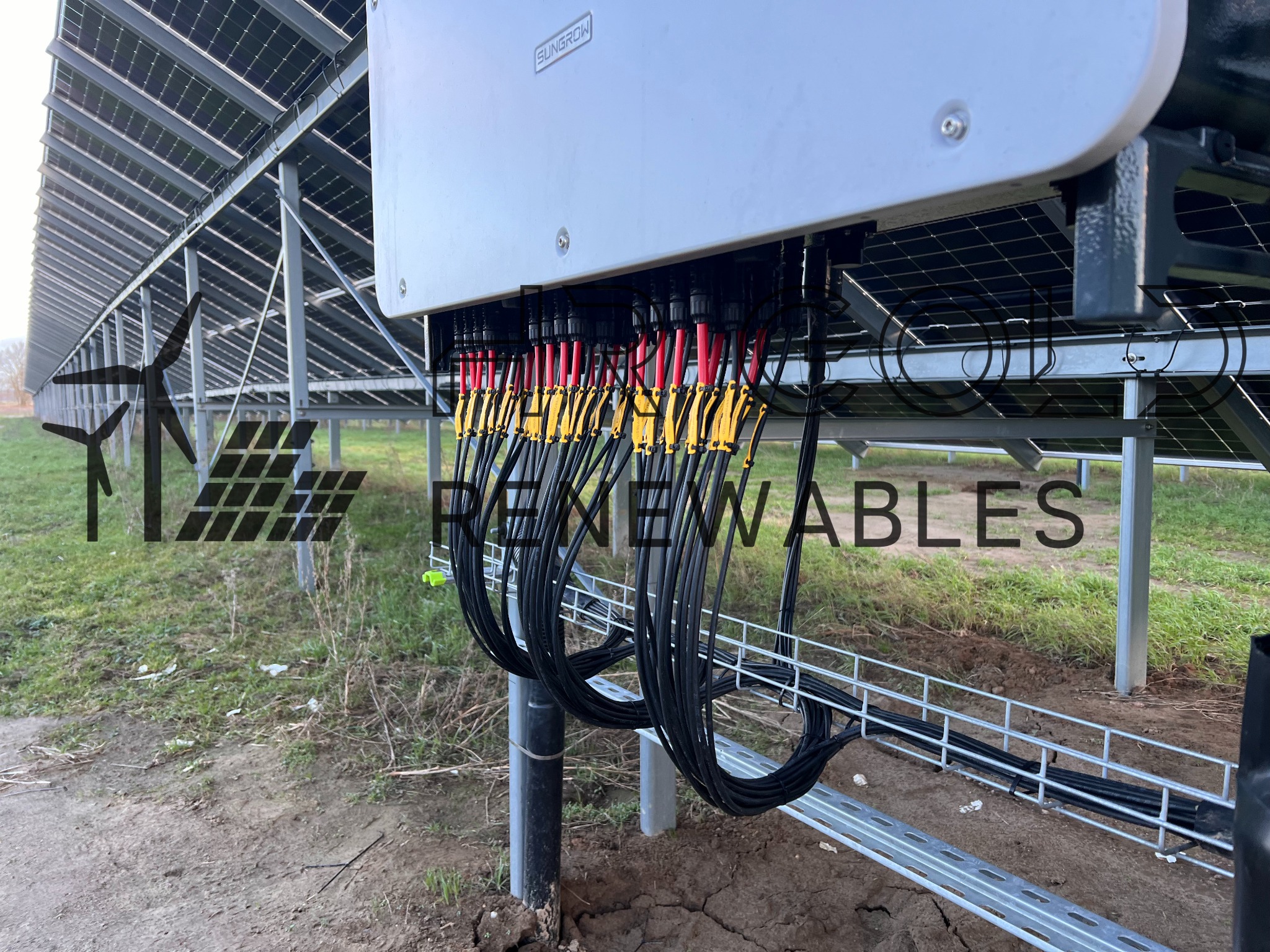 Inwerter fotowoltaiczny Sungrow z podłączonymi kablami, widok z dołu, instalacja paneli słonecznych w tle.