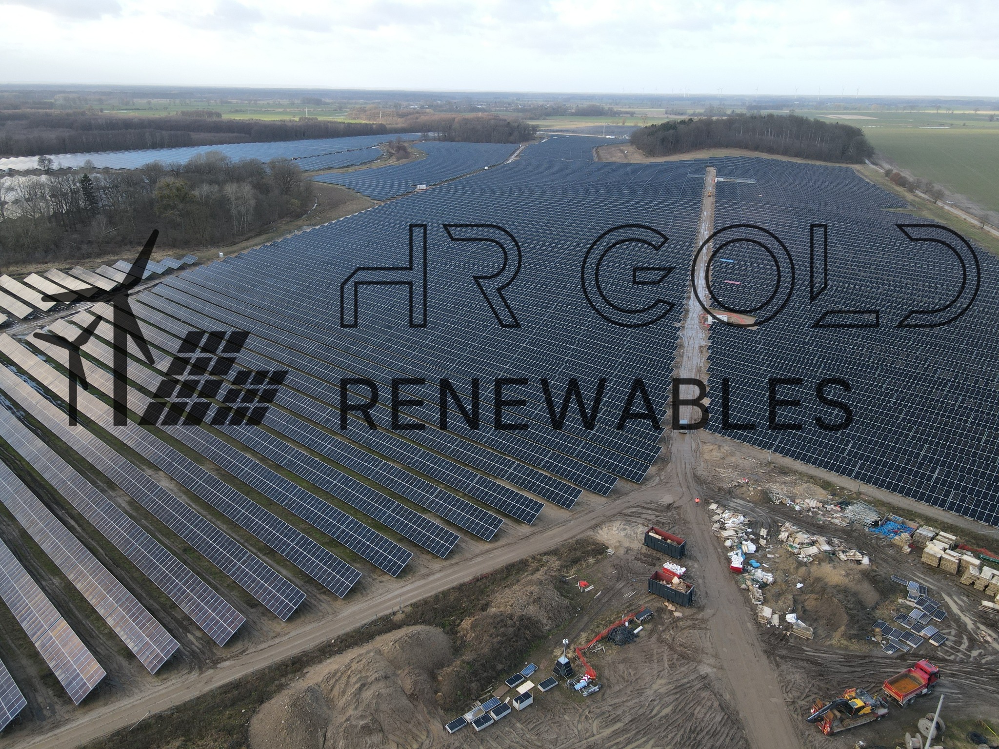 Rozległa farma paneli słonecznych z turbiną wiatrową w tle, widok z lotu ptaka, z widocznym logiem firmy HR Gold Renewables.