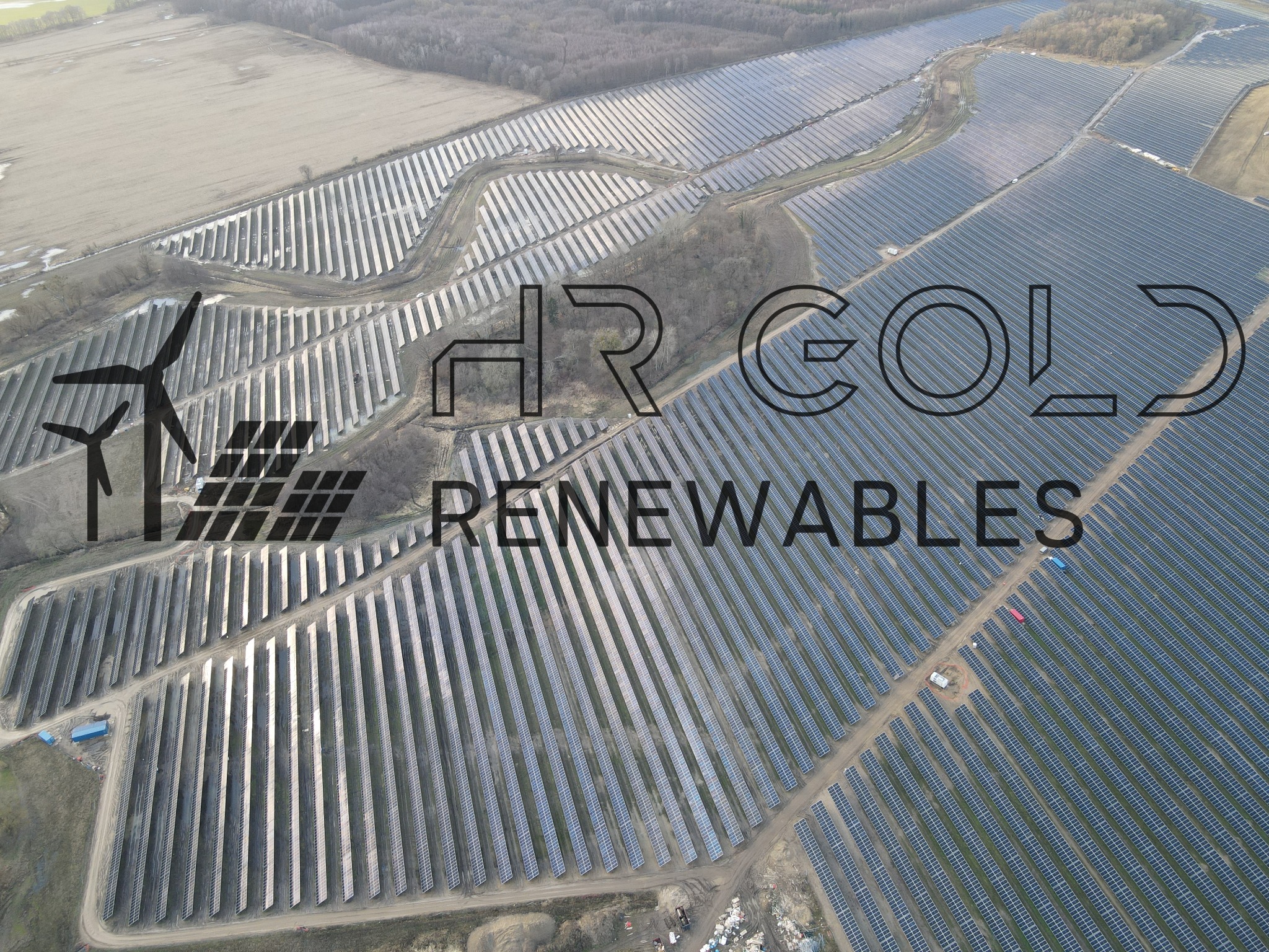 Widok z lotu ptaka na farmę fotowoltaiczną z turbiną wiatrową w tle, logo firmy HR Gold Renewables na pierwszym planie.