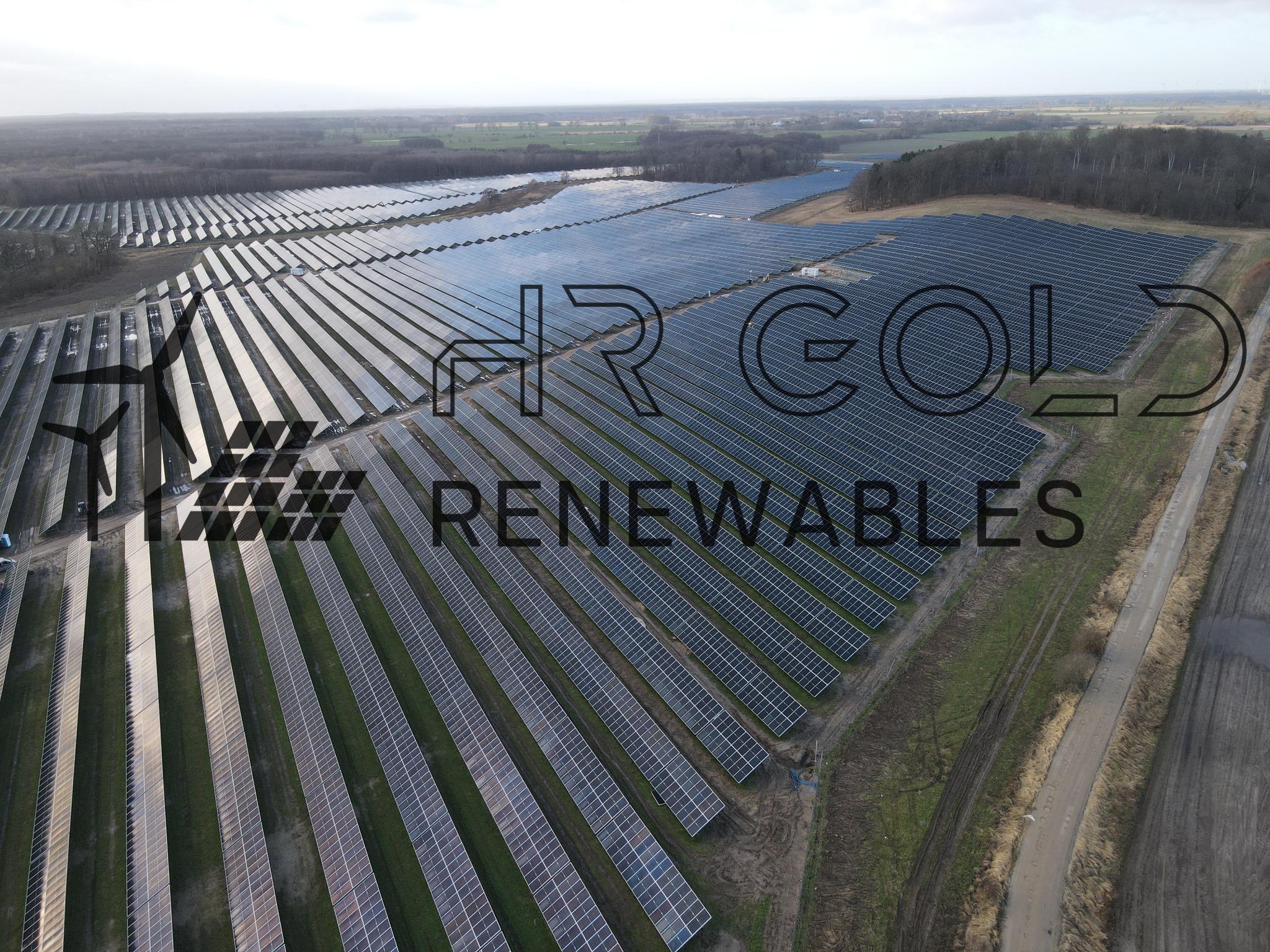 Rozległa farma paneli słonecznych widziana z lotu ptaka, z lasem w tle i logo firmy HR Gold Renewables nałożonym na obraz.