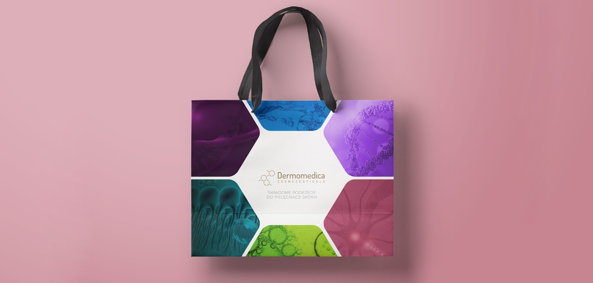 Torba z nadrukiem firmowym Dermomedica, prezentująca logo i abstrakcyjne grafiki w kształcie plastrów miodu na różowym tle.