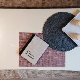 Widok z góry na biały stolik kawowy z książką o projektowaniu wnętrz, podkładką i dekoracyjną tacą z dwoma świecami i kulą.