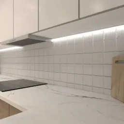 Nowoczesna kuchnia z białymi szafkami, marmurowym blatem, płytą indukcyjną i drewnianymi deskami do krojenia opartymi o ścianę z białych kwadratowych płytek.