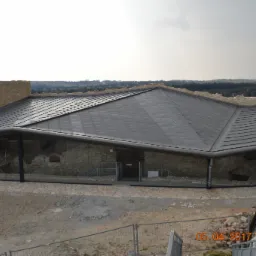 Zadaszenie nad ruinami zamku w Rabsztynie, widok z góry na nowoczesną konstrukcję z metalowym dachem i szklanymi ścianami, chroniącą kamienne pozostałości średniowiecznej budowli.