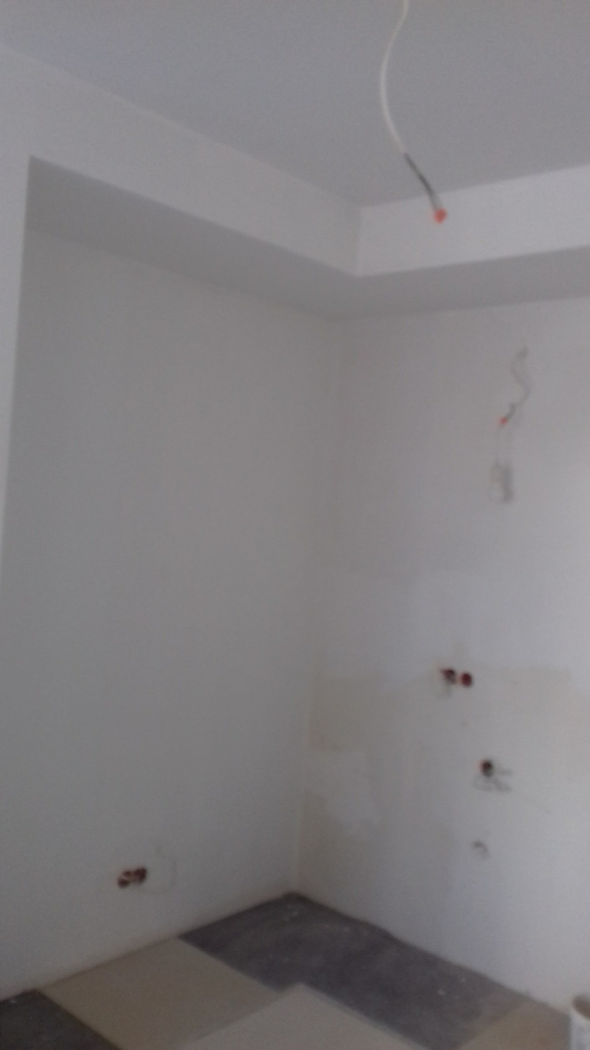 Wnętrze w trakcie prac wykończeniowych: białe ściany, częściowo ułożona podłoga z płytek w odcieniach szarości i beżu, wystające kable elektryczne.