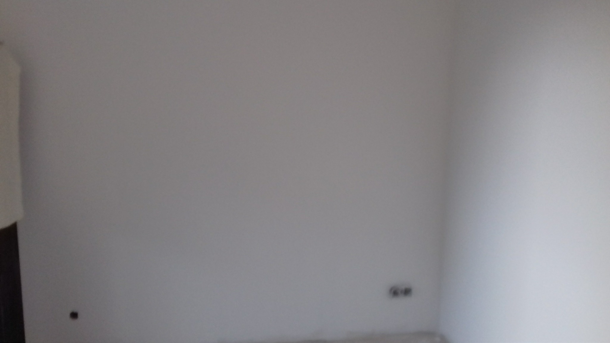 Pomalowana na szaro ściana w rogu pokoju z widocznymi gniazdkami elektrycznymi i fragmentem podłogi.