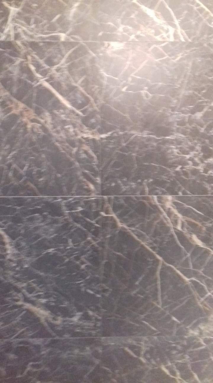 Ściana wyłożona ciemnymi płytkami imitującymi marmur z jasnymi żyłami, widoczne fugi.