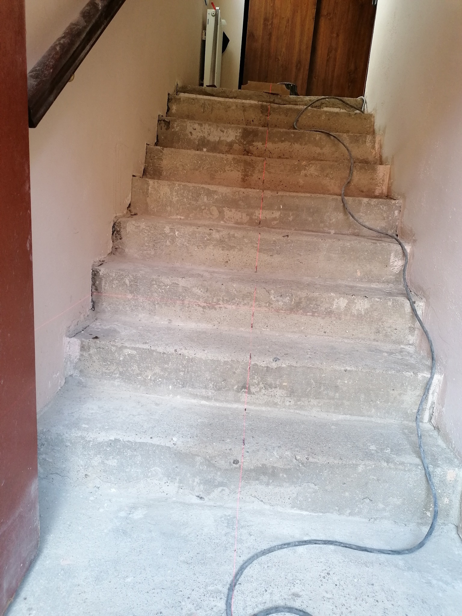 Betonowe schody w trakcie remontu, widoczna linia lasera wyznaczająca poziom, kabel elektryczny leżący na stopniach.