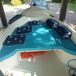 Wnętrze łodzi z nową, turkusową tapicerką: poduszki w granatowe kropki, wałki tapicerowane, pomarańczowa lina w schowku.