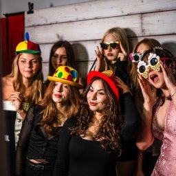 Art Foto Katarzyna Margol - Grupa kobiet w zabawnych przebraniach pozuje do zdjęcia w fotobudce. Kolorowe kapelusze, okulary i radosne miny tworzą wesołą atmosferę imprezy.