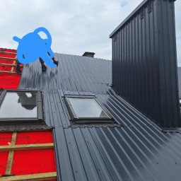Bogacki sp. z o.o. - Montaż blachy na dachu z oknami połaciowymi i kominem. Widoczna czerwona membrana dachowa i narzędzia pracy. Praca w toku, widok z góry.