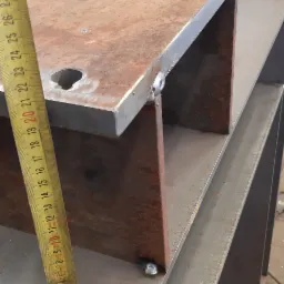 Metalowa konstrukcja spawana z blachy i profili, widoczne spawy, obok miarka zwijana, w tle warsztat.