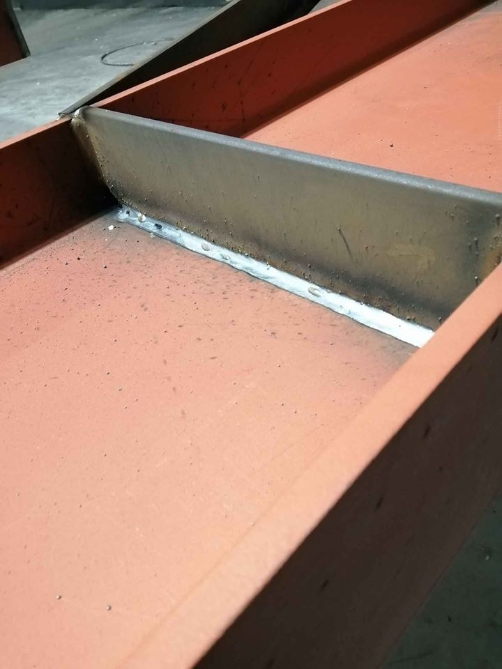 Spoina łącząca stalowe elementy konstrukcji pomalowane na czerwono-pomarańczowo, widoczne ślady spawania