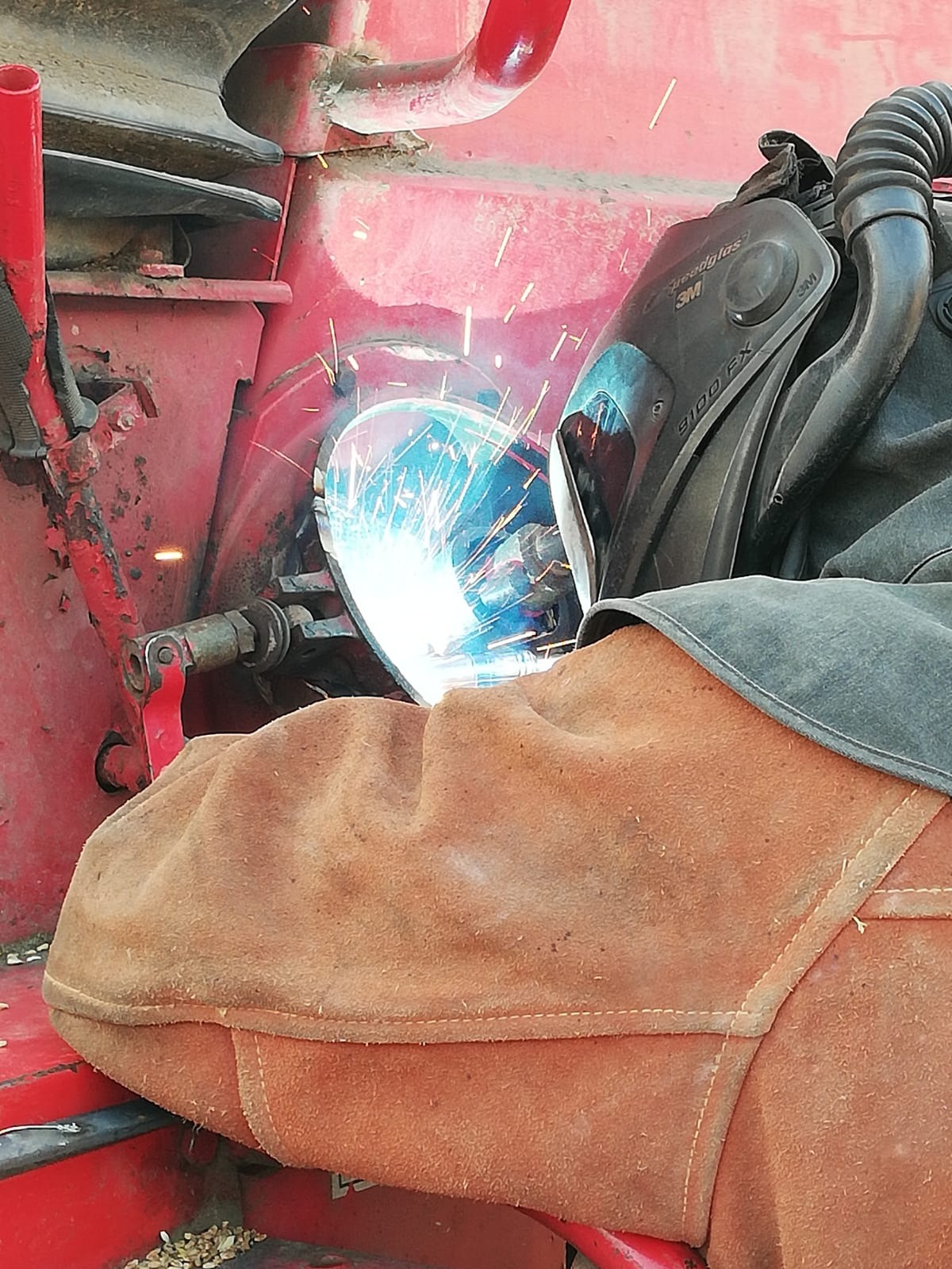 Spawanie elementu czerwonej maszyny rolniczej z użyciem maski spawalniczej 3M Speedglas 9100 FX i ochronnego skórzanego rękawa.