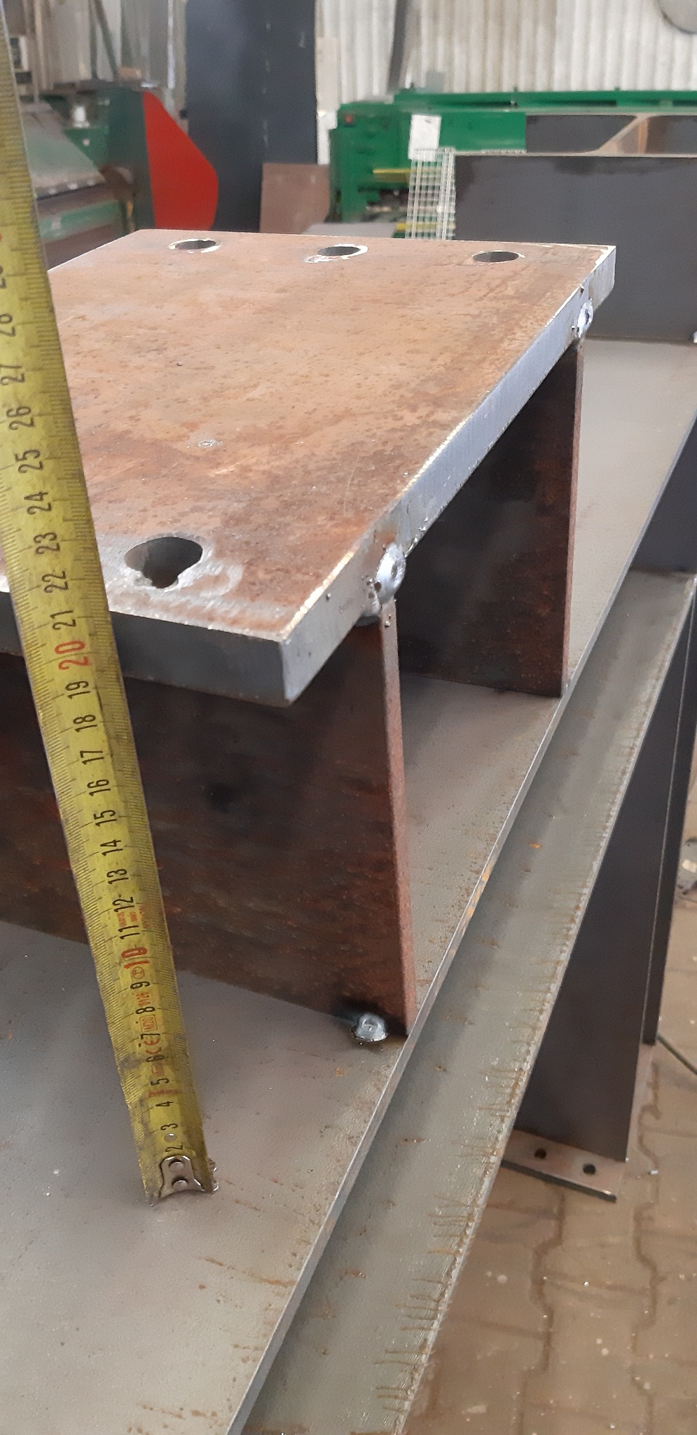 Metalowa konstrukcja spawana z blachy i profili, widoczne spawy, obok miarka zwijana, w tle warsztat.