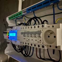 GT-Instel INSTALACJE ELEKTRYCZNE - Rozdzielnica elektryczna z licznikiem i gniazdem, widoczne bezpieczniki Eaton, przewody w kolorach: czarnym, niebieskim, żółto-zielonym. Oświetlenie LED licznika.