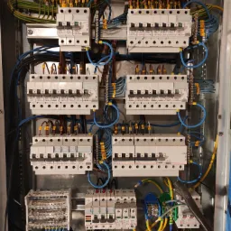 Rozdzielnica elektryczna z licznymi bezpiecznikami Legrand, okablowaniem oznaczonym numerami i kolorami, widok z bliska na wewnętrzne komponenty szafy sterowniczej.