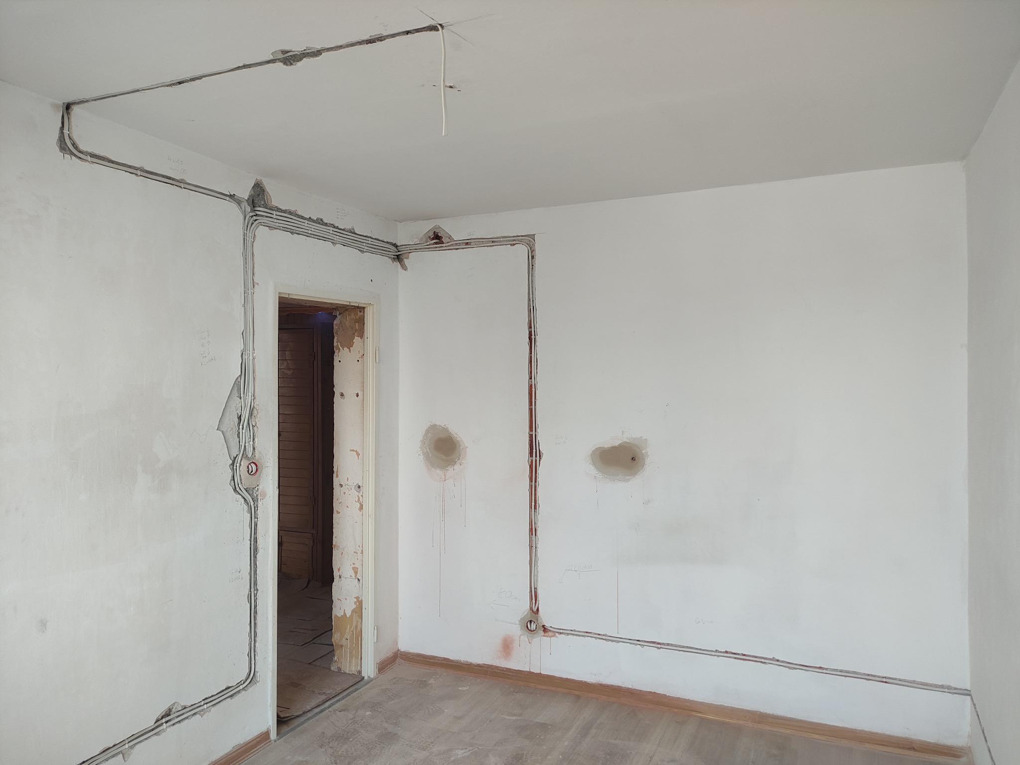 Wnętrze w trakcie remontu z widoczną instalacją elektryczną w bruzdach ściennych i sufitowych, przygotowaną do dalszych prac wykończeniowych. Widoczne kable i puszki.