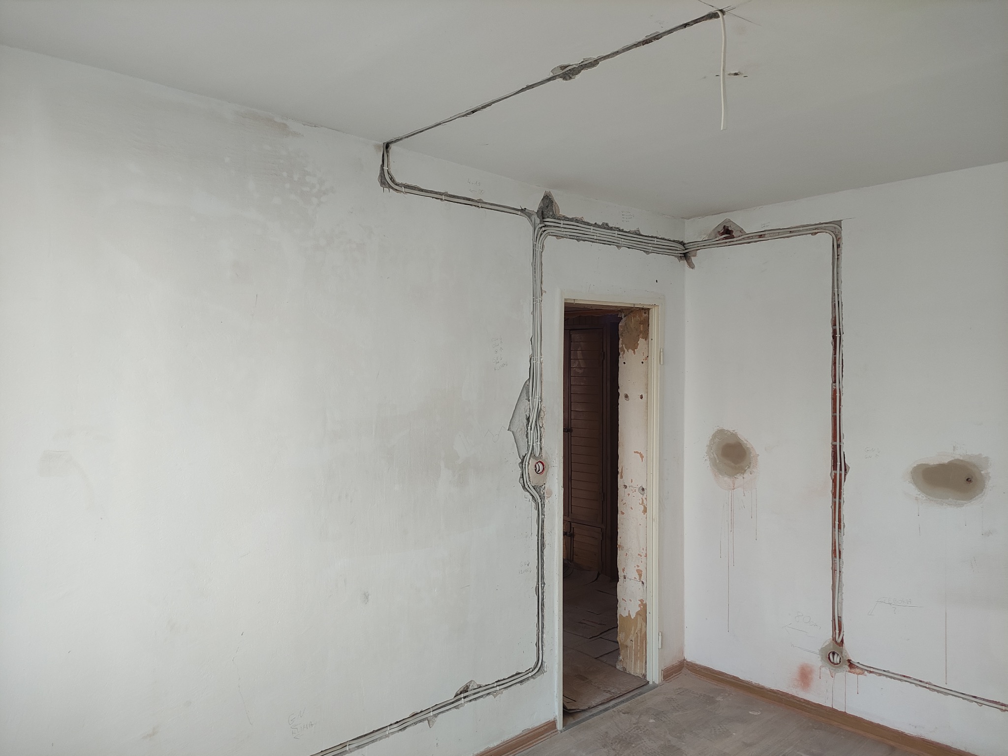 Ściana w trakcie remontu z widocznymi przewodami elektrycznymi ułożonymi w bruzdach, przygotowanymi do dalszych prac wykończeniowych. Widoczne puszki elektryczne.