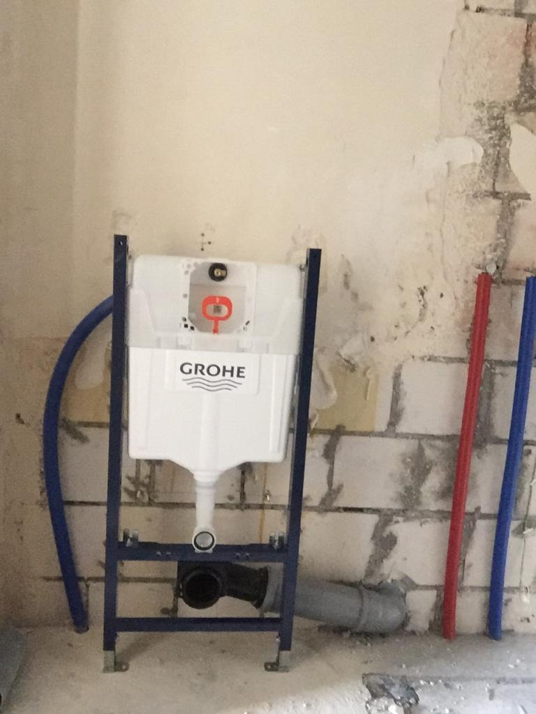 Stelaż podtynkowy Grohe zamontowany na surowej ścianie z widocznymi instalacjami wodnymi i kanalizacyjnymi przed zabudową.