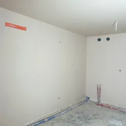 Wnętrze w Lesznie w trakcie prac wykończeniowych: ściany przygotowane pod malowanie, widoczne instalacje elektryczne i hydrauliczne zabezpieczone folią.