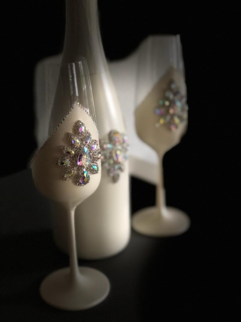 Elegancki, biały zestaw prezentowy z butelką i dwoma kieliszkami ozdobionymi błyszczącymi kamieniami, oferowany przez firmę z Czaplinka. Idealny na wyjątkowe okazje.