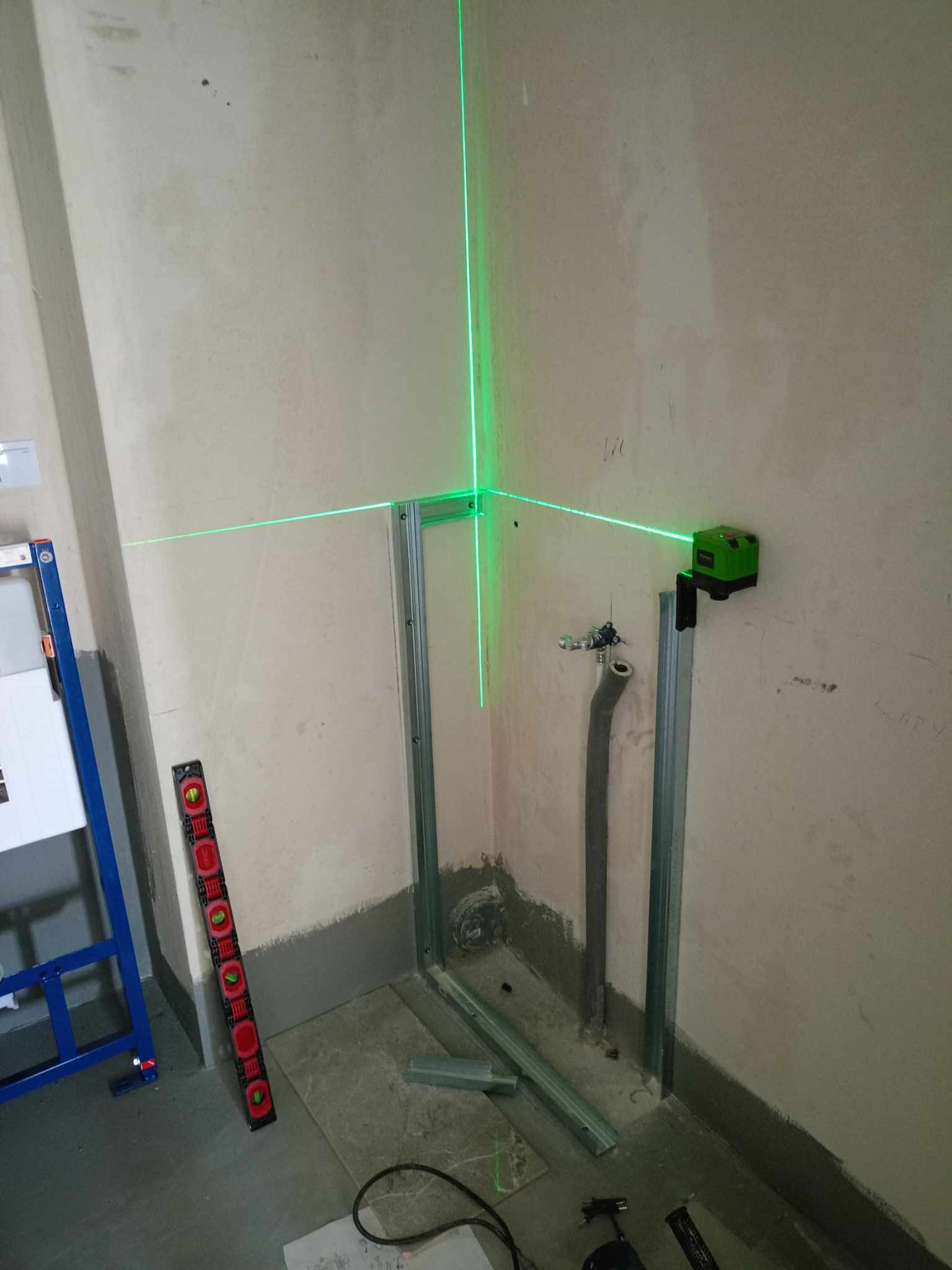 Montaż stelaża podtynkowego WC z użyciem poziomicy laserowej, widoczne profile metalowe, rury i poziomica tradycyjna.