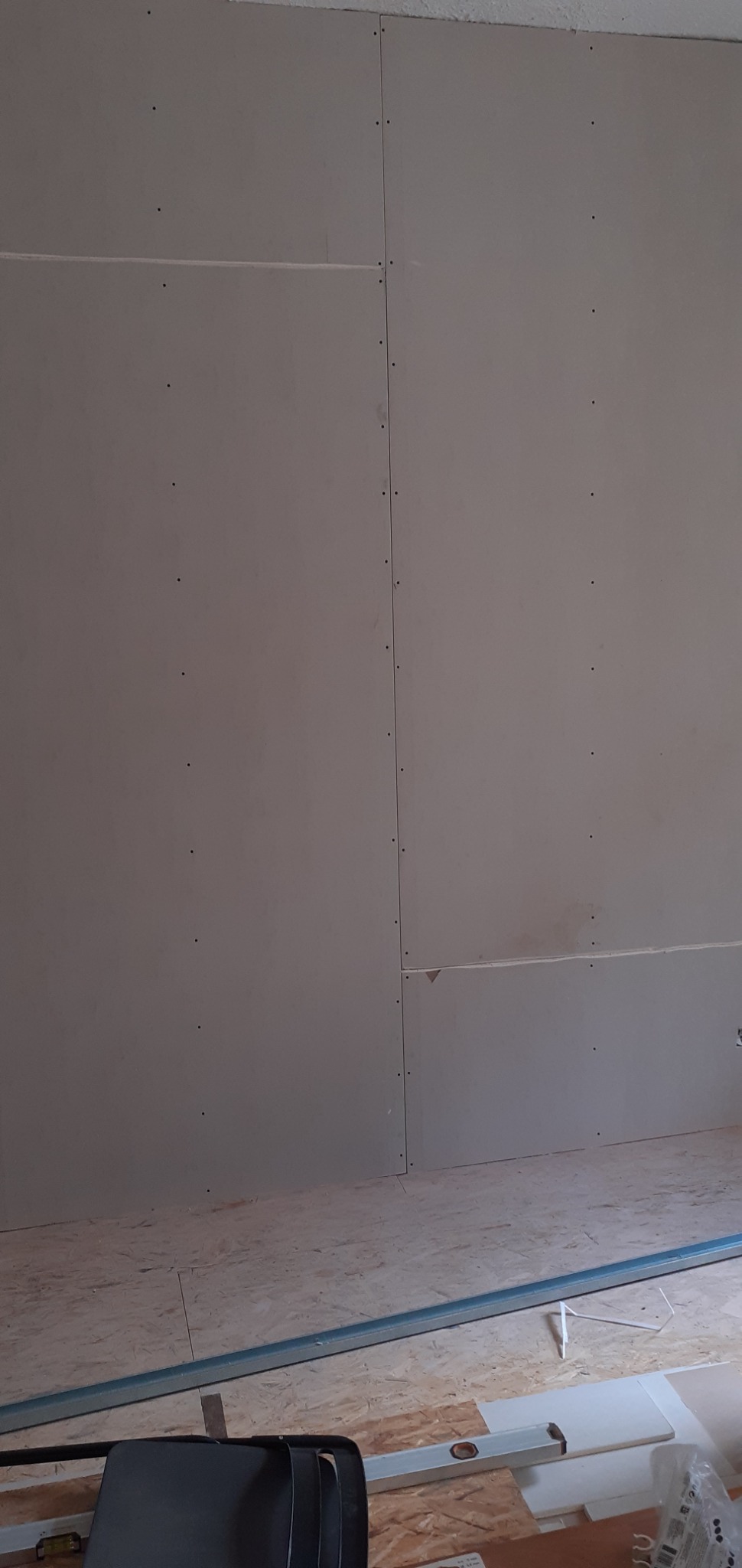 Ściana z płyt kartonowo-gipsowych, widoczne łączenia i miejsca wkrętów, na podłodze płyty OSB i profil metalowy.