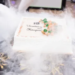 Tort urodzinowy z dekoracją i napisem '18 Urodziny Kacpra', otoczony efektem suchego lodu, na stole z dekoracyjnym wzorem w Pleszewie.