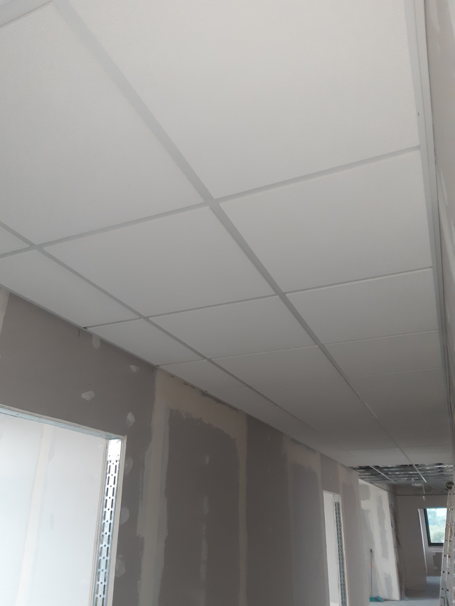 Montaż sufitu podwieszanego kasetonowego z widoczną konstrukcją nośną i przygotowanymi do szpachlowania ścianami w trakcie prac wykończeniowych.