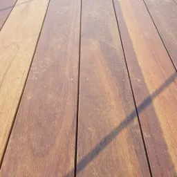 Szczegółowe ujęcie desek tarasowych z egzotycznego drewna tekowego, widoczne śruby mocujące i cień padający na powierzchnię.