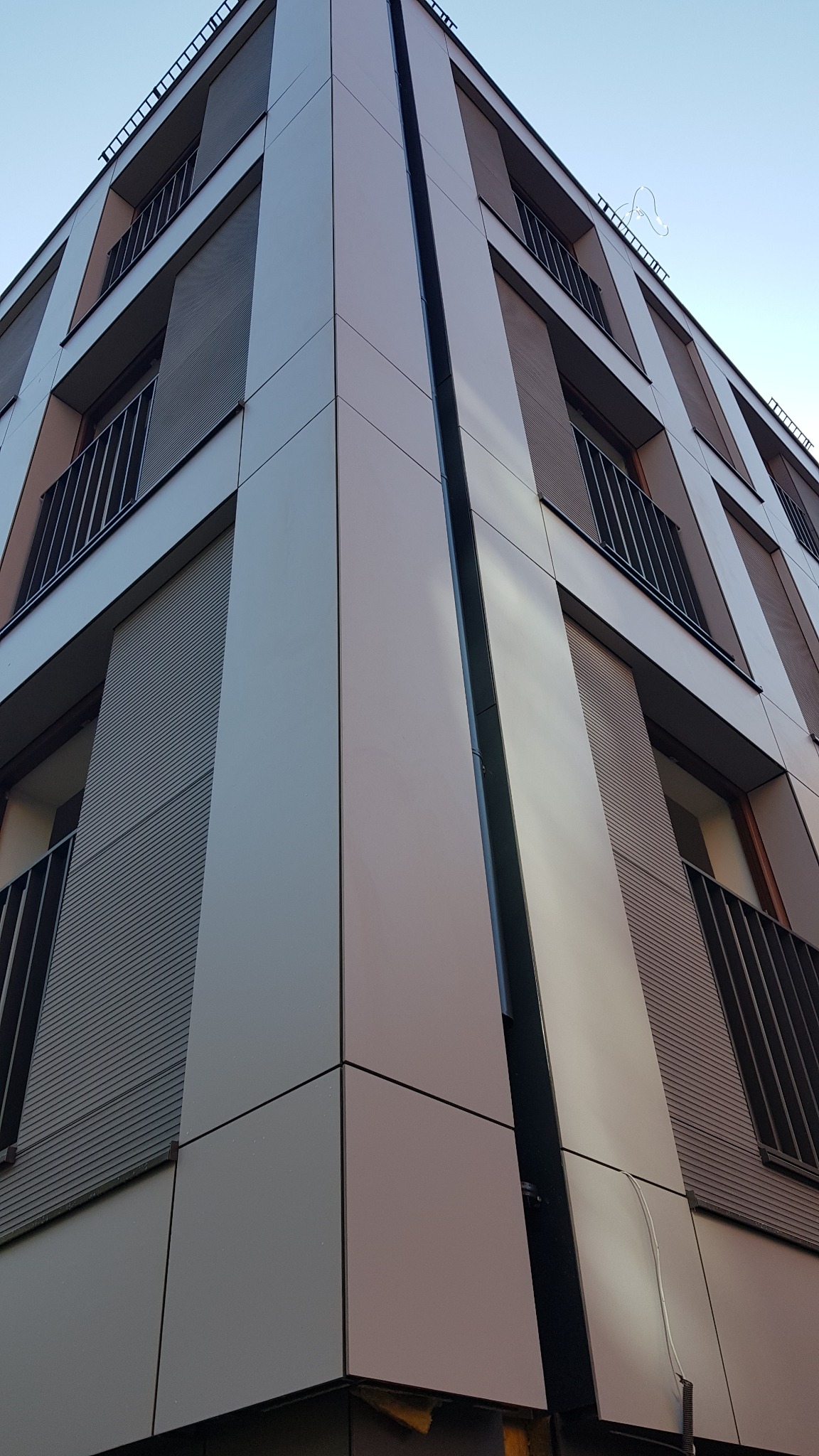 Elewacja wentylowana budynku wielorodzinnego w Gdyni, z widocznymi panelami elewacyjnymi i balkonami z metalowymi barierkami, sfotografowana z dołu pod kątem.