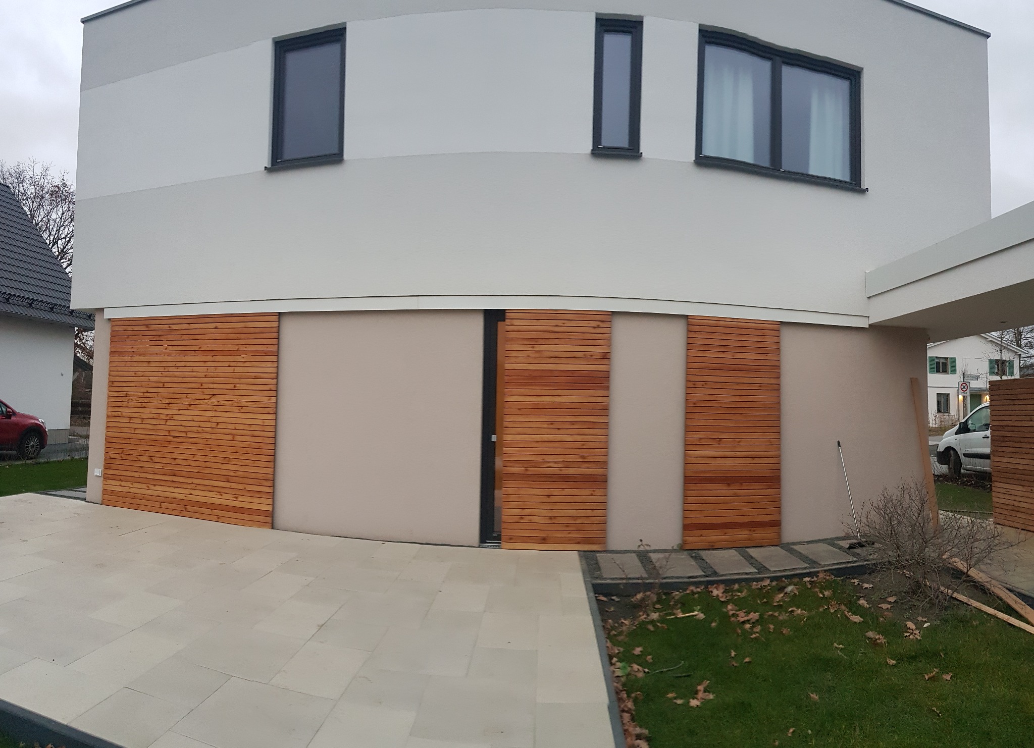 Nowoczesny dom z przesuwnymi roletami z modrzewiowego drewna olejowanego na aluminiowej konstrukcji, widoczne z zewnątrz na tle jasnej elewacji i kamiennej ścieżki.