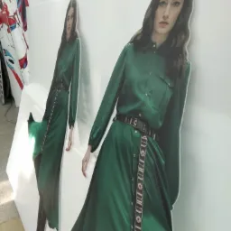 Dwie wycięte z płyty postacie kobiety w długiej, zielonej sukience, ustawione obok siebie na białym tle, widoczne z boku.